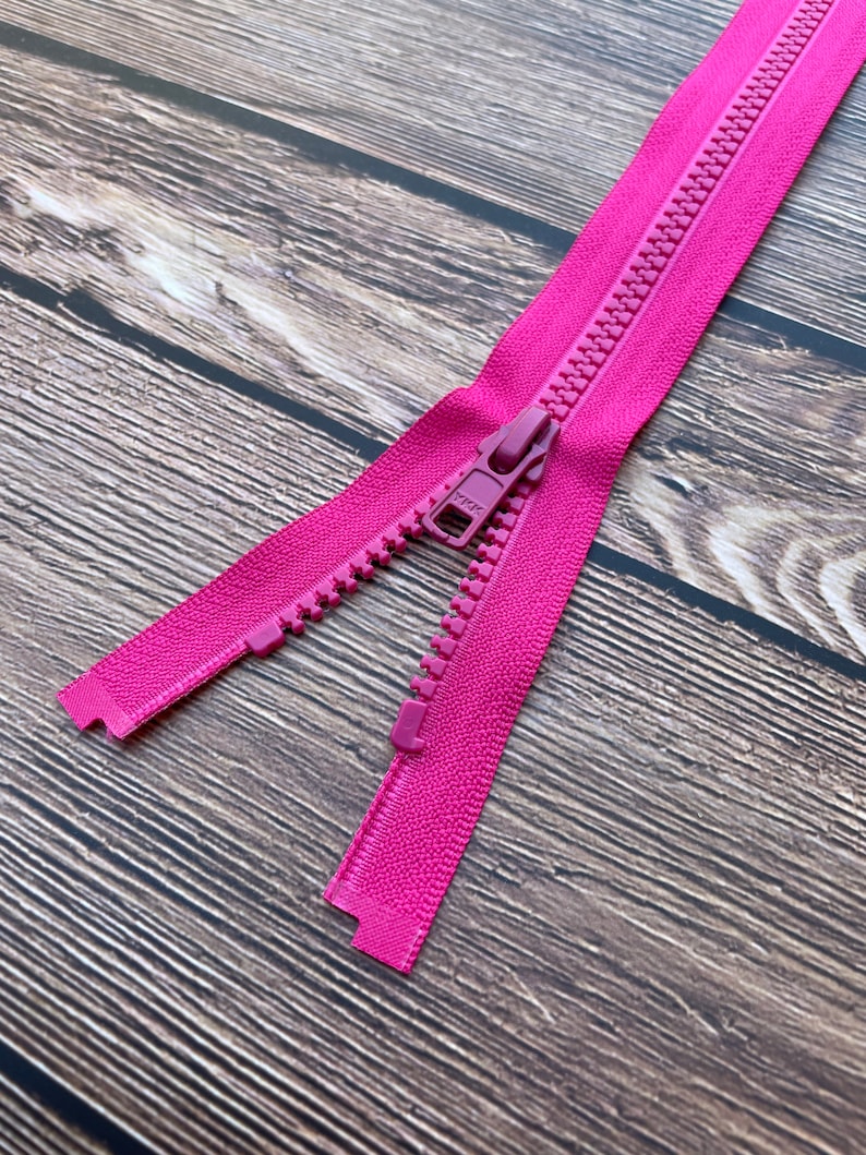May include: A pink zipper with a metal slider. The zipper is open and the slider is in the middle of the zipper.