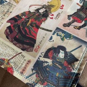 Può includere: Un pannello di tessuto con un design a patchwork che presenta più immagini di guerrieri samurai giapponesi in abiti tradizionali. Il tessuto è beige con cuciture di colore blu chiaro attorno ai bordi.
