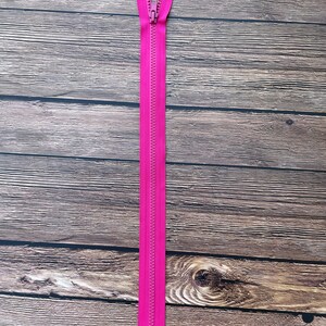 May include: A pink zipper with a metal slider. The zipper is lying flat on a wooden surface.