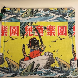 以下が含まれることがあります： 冒険のテーマの黄色い布製のポーチ。帽子をかぶった猫が釣り竿を持ってボートに乗っています。猫の後ろには魚が飛び跳ねています。ポーチには「冒険 冒険」と日本語で書かれています。