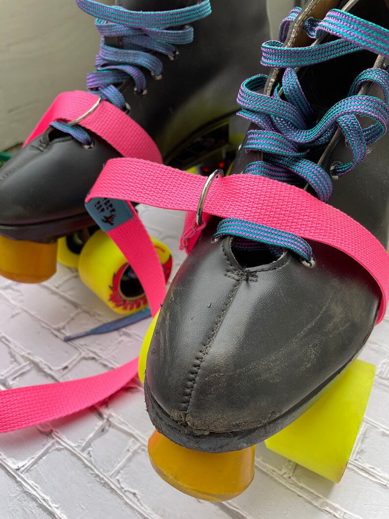 Puede incluir: Patines de ruedas de cuero negro con ruedas amarillas y correas rosas. Los cordones son de color turquesa y morado.