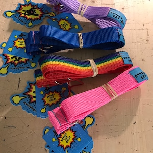 Puede incluir: Cuatro correas para perros de colores con un dise&ntilde;o de arco&iacute;ris, rosa, azul y morado. Cada correa tiene un clip de metal y una etiqueta que dice "Attack Cat Bags!" con un gr&aacute;fico de un gato de dibujos animados.