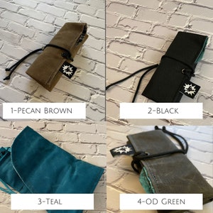 K&ouml;nnte beinhalten: Vier verschiedene Farben von Stoff-Bleistiftetuis. Die Farben sind Pecanbraun, Schwarz, Teal und Olivgr&uuml;n. Jedes Etui hat einen schwarzen Riemen und ein kleines wei&szlig;es Logo.