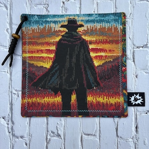 May include: Square tapestry featuring a silhouette of a figure in a hat and cloak against a sunset backdrop of red, orange, and yellow hues. The tapestry has a black cord and wooden bead attached to the top corner.