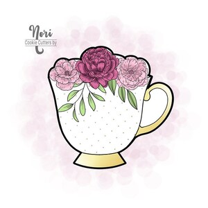 May include: A cookie cutter in the shape of a teacup, decorated with pink and burgundy flowers and green leaves. The teacup is white with gold accents and small gold dots. The text "Nori Cookie Cutters by" is in the upper left corner.