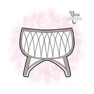 May include: A cookie cutter in the shape of a bassinet. The bassinet is light gray with a black outline and a decorative lattice design. The text "Nori Cookie Cutters by" is in the upper right corner.