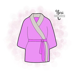 May include: A pink bathrobe cookie cutter with a gray trim and a tied sash. Nori Cookie Cutters by is written in the top right corner of the image.