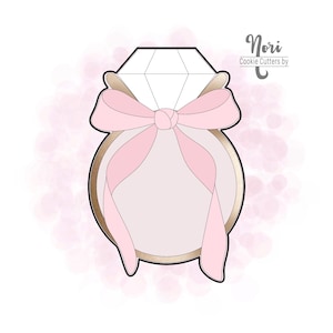 May include: A cookie cutter in the shape of a diamond ring with a pink bow. The ring is gold-colored with a large, faceted diamond shape at the top. The bow is a soft pink color and is tied around the ring.
