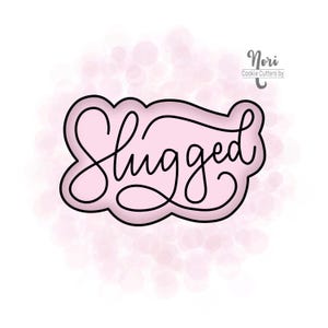 May include: A pink cookie cutter with a black outline in the shape of a cloud with the word "Hugged" written in cursive inside.