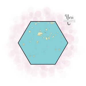 May include: A turquoise blue hexagonal cookie cutter with a gold glitter design. The cookie cutter is on a white background with a pink watercolor effect.