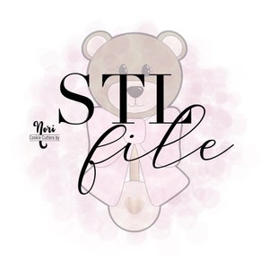 May include: A pink and brown cookie cutter in the shape of a teddy bear wearing a bow tie. The text "STi file" is written in black cursive above the bear.