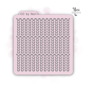 May include: A light pink cookie stencil with a gray knit pattern. The stencil has rounded corners and the text "CC by Nori" is printed on the top left. The brand name "Nori Cookie Cutters by" is printed on the top right.