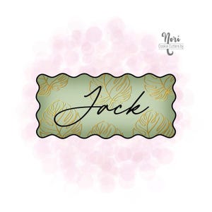 May include: A green cookie cutter with a wavy edge and a gold leaf pattern. The name "Jack" is written in black cursive script on the cutter.