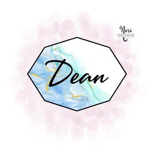 May include: A hexagonal cookie cutter with a blue and gold marble design. The cutter is outlined in black and has the name "Dean" written in black inside. The background is a soft pink with white dots.