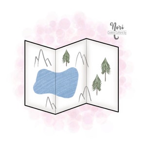May include: A white, folded map-shaped cookie cutter with a black outline. The map design includes a blue lake, grey mountains, and green trees. The text "Nori Cookie Cutters by" is in the upper right corner.