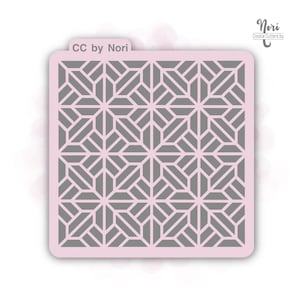 May include: A pink plastic stencil with a geometric pattern of gray squares and rectangles. The stencil is labeled "CC by Nori" in the top left corner and "Nori Cookie Cutters by" in the top right corner.