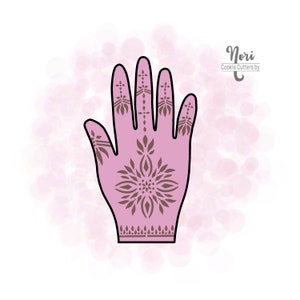 May include: A pink hand with a detailed brown henna design. The design features a large central flower with smaller flowers and geometric patterns on the fingers and wrist. The text "Nori Cookie Cutters by" is in the upper right corner of the image.