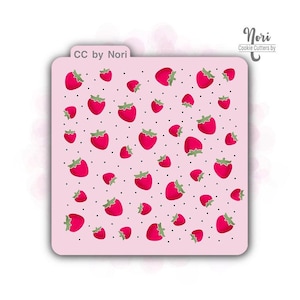 May include: Pink cookie stencil with a repeating pattern of red strawberries and black polka dots. The stencil has the text "CC by Nori" and "Nori Cookie Cutters by" printed on it.