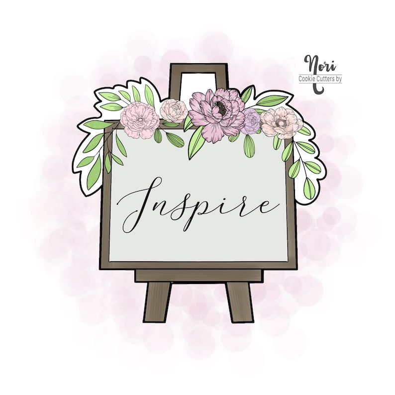 May include: A cookie cutter in the shape of an artist's easel with the word "Inspire" written on the canvas. The easel is decorated with flowers and leaves in shades of pink, purple, and green. The cookie cutter is from Nori Cookie Cutters.