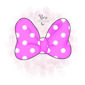 May include: A pink bow-shaped cookie cutter with white polka dots. The cookie cutter has a black outline and the text "Nori Cookie Cutters by" in a script font.