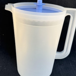 May include: A translucent white plastic pitcher featuring a sturdy handle and a pouring spout. The pitcher includes a removable light blue circular lid with a small central knob for easy lifting, providing a functional design for liquid storage.