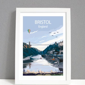 Peut inclure: Une affiche encadrée représentant une vue de Bristol, en Angleterre. L'œuvre d'art montre une scène de rivière avec un pont, des bâtiments et une montgolfière sur fond de ciel bleu clair. Le mot "BRISTOL" est imprimé en haut.