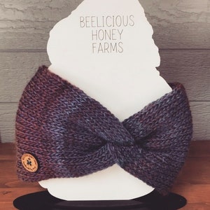 May include: A purple and blue knitted headband with a wooden button featuring a paw print and the text "Beelicious Honey Farms".