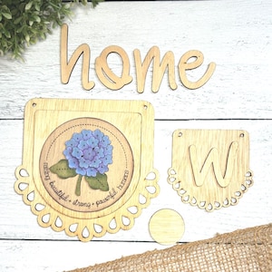 May include: Wooden home decor sign with the word "home" in cursive, a banner with a hydrangea flower and the text "raising beautiful, strong, & powerful humans", and a banner with the letter "W".