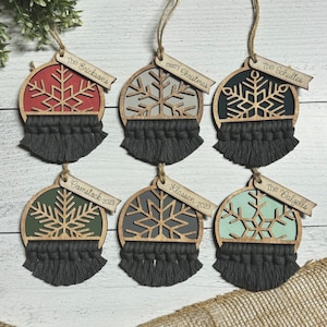 May include: Six round wooden baubles with a snowflake design and a black tassel. Each bauble has a personalised tag with a name and year. The baubles are painted in various colours, including red, grey, black, green, and light blue.
