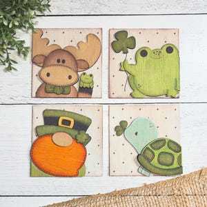 May include: Four wooden signs with a white background and green, brown, and orange painted designs. The signs feature a moose, a frog, a leprechaun, and a turtle.