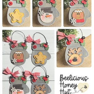 May include: Six wooden Christmas ornaments shaped like mittens with different designs. The designs include a snowman, a gingerbread person, a reindeer, and a star. The ornaments are decorated with red and white gingham ribbon and green holly. The text "Beelicious Honey Hut" is at the bottom of the image.