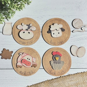 May include: Wooden farm animal sound matching game with four circular pieces. Each piece features a different farm animal, including a cow, sheep, pig, and chicken. The animals are painted in bright colors and have cute expressions. Each piece also has the animal's sound written below the image. The game includes additional pieces for each animal, such as a milk bottle for the cow, a ball of yarn for the sheep, a pile of mud for the pig, and two eggs for the chicken.