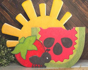 May include: A wooden sun, watermelon slice, strawberry, and ant cutout. The sun is yellow, the watermelon is red and green, the strawberry is red and green, and the ant is black.