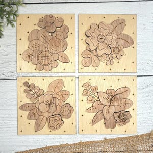 Peut inclure: Quatre carrés en bois avec des motifs floraux découpés au laser. Chaque carré présente un arrangement différent de fleurs et de feuilles, avec des détails complexes et des motifs de couture.