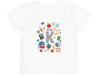 May include: A white short-sleeved t-shirt featuring a central graphic with the text 'pre-K' in a large gray letter K. The design includes colorful illustrations of school supplies like an apple, globe, backpack, books, pencils, and sports balls.