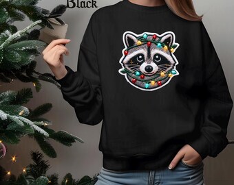 May include: Black sweatshirt featuring a raccoon wearing Christmas lights. The raccoon has a gray and white face with large eyes and a black nose. The sweatshirt has the word "Black" printed at the top.