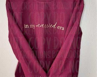 May include: Burgundy sweatshirt with the text "in my married era" in gold script. The year "2015" and "Mrs. Papp" are embroidered on the sleeve. The sweatshirt is hanging on a black hanger.