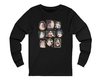 May include: Black long-sleeve shirt featuring a whimsical design of cartoon ghosts reading books within ornate frames. The ghosts are depicted in various poses, with books of different colors. The design is centered on the shirt.
