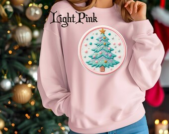 May include: Light pink sweatshirt with a round Christmas tree design. The tree is teal with glitter accents, a gold star, and colorful ornaments. The text "Light Pink" is above the design.