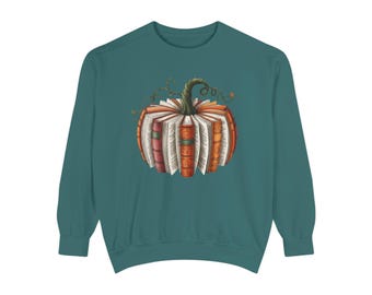 May include: Teal sweatshirt featuring a pumpkin design made of books. The pumpkin is orange with a green stem and vines. The books have various colors and textures, creating a unique fall-themed graphic.