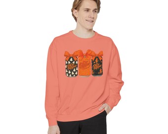 May include: Coral-colored sweatshirt featuring a graphic of three Dr. Pepper cans with Halloween-themed designs and orange bows. The cans have patterns of ghosts, pumpkins, and witches. The sweatshirt is long-sleeved.