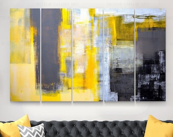May include: Abstract art piece in shades of yellow, gray, and black, divided into five panels. The artwork features brushstroke textures and geometric shapes. The piece is displayed above a dark gray tufted sofa with yellow and patterned pillows.