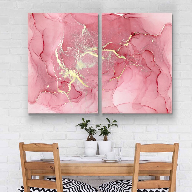 May include: Two pink abstract paintings with gold accents. The paintings are framed and hung on a white brick wall.