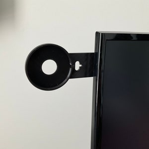 Puede incluir: Soporte de c&aacute;mara web negro fijado al lateral de un monitor de ordenador negro.