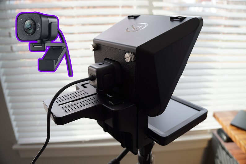 May include: A black webcam and teleprompter setup. The webcam is mounted on a stand, and the teleprompter has a screen. The setup is designed for video recording and streaming.