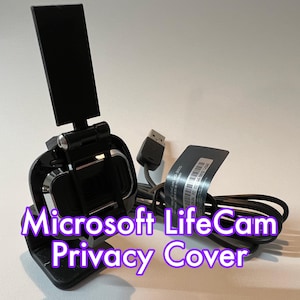 May include: A black Microsoft LifeCam privacy cover with a sliding cover to protect the camera lens. The cover is attached to a small black stand with a USB cable.