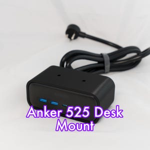 May include: A black Anker 525 Desk Mount with three blue USB ports. The device has a black power cord and plug. The text "Anker 525 Desk Mount" is displayed in a purple font.