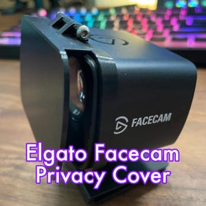 May include: A black Elgato Facecam privacy cover. The cover is rectangular with rounded edges and features the word "FACECAM" in white. The text "Elgato Facecam Privacy Cover" is displayed in a purple font.