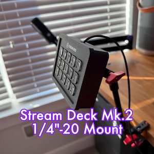 May include: A black Stream Deck Mk.2 with 15 buttons is mounted on a 1/4"-20 mount. The mount is attached to a black arm with a red clamp.