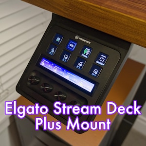 May include: A black Elgato Stream Deck Plus mounted to a wooden desk. The Stream Deck has a blue LCD screen and several buttons with icons for various functions, including "Home", "Head", "Music", and "Monitor Mic".